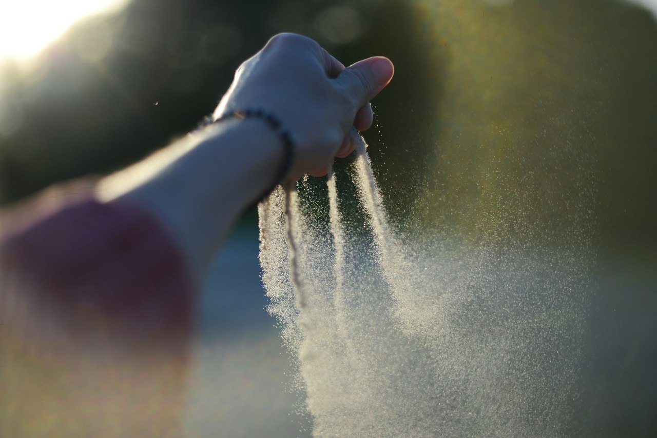 Sand rinnt durch eine Hand im warmen Gegenlicht der Sonne.